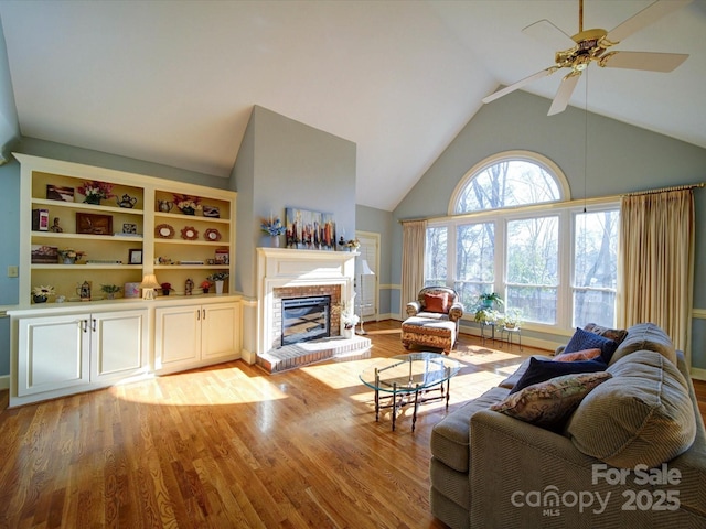 living room with vaulted ceiling, light hardwood / wood-style flooring, a brick fireplace, and ceiling fan