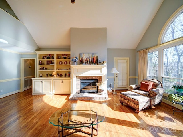 living room featuring built in features, high vaulted ceiling, light hardwood / wood-style floors, and a brick fireplace