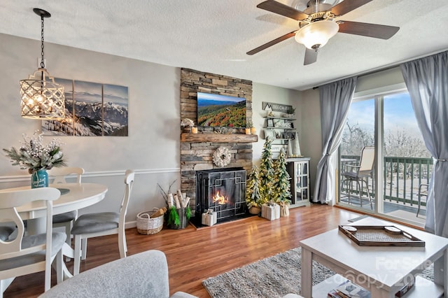 living room featuring a textured ceiling, hardwood / wood-style flooring, a stone fireplace, and ceiling fan