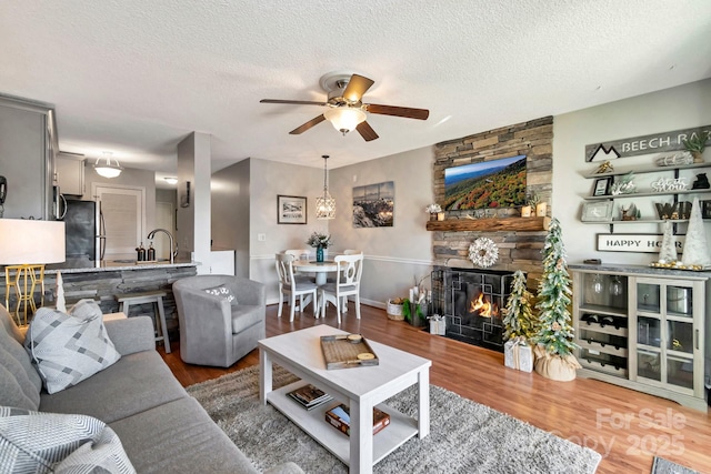 living room featuring a stone fireplace, sink, hardwood / wood-style flooring, ceiling fan, and a textured ceiling