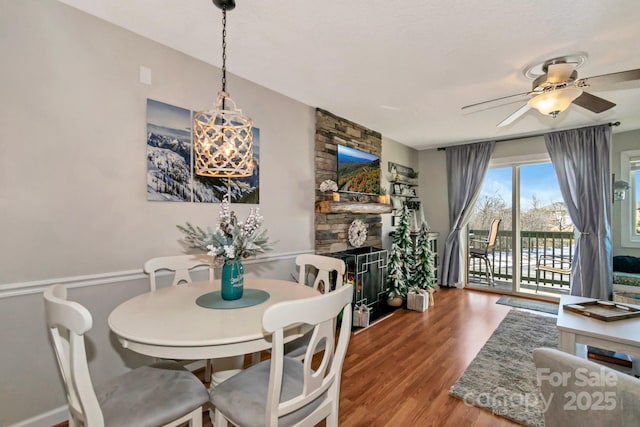 dining area featuring a stone fireplace, ceiling fan, and hardwood / wood-style floors