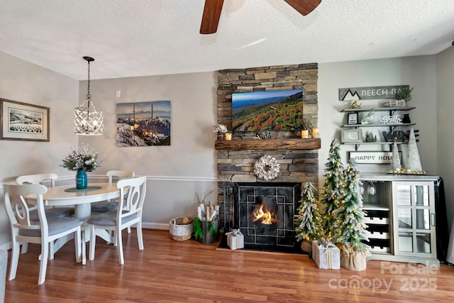 dining area featuring hardwood / wood-style floors, a textured ceiling, a stone fireplace, and ceiling fan