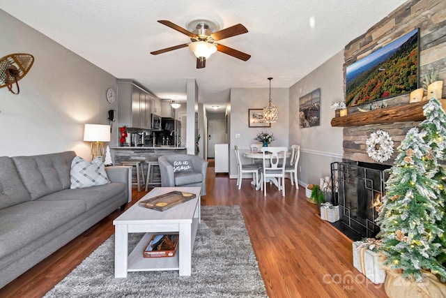 living room featuring a textured ceiling, a stone fireplace, ceiling fan, and dark wood-type flooring