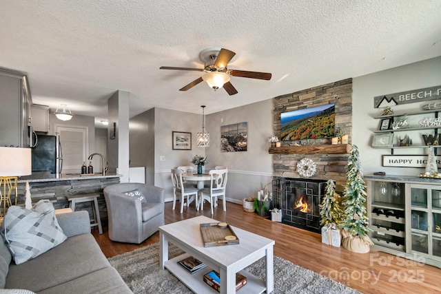 living room with a textured ceiling, ceiling fan, sink, wood-type flooring, and a fireplace