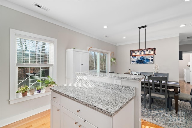 kitchen featuring light wood-type flooring, crown molding, pendant lighting, white cabinets, and a center island