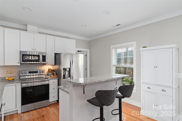 kitchen featuring a center island, a kitchen breakfast bar, light hardwood / wood-style floors, white cabinetry, and stainless steel appliances