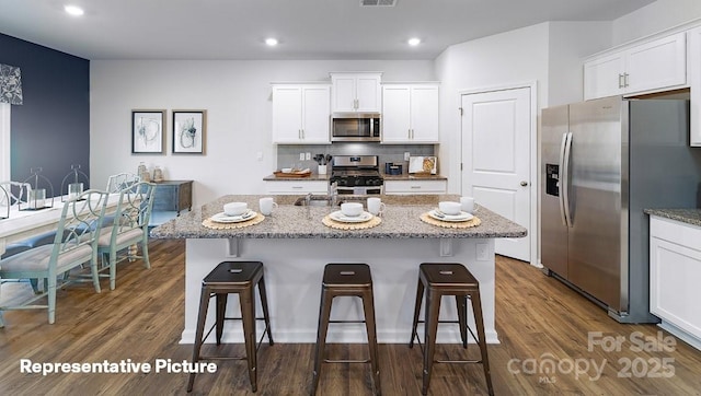 kitchen featuring white cabinetry, a kitchen island with sink, light stone counters, and appliances with stainless steel finishes