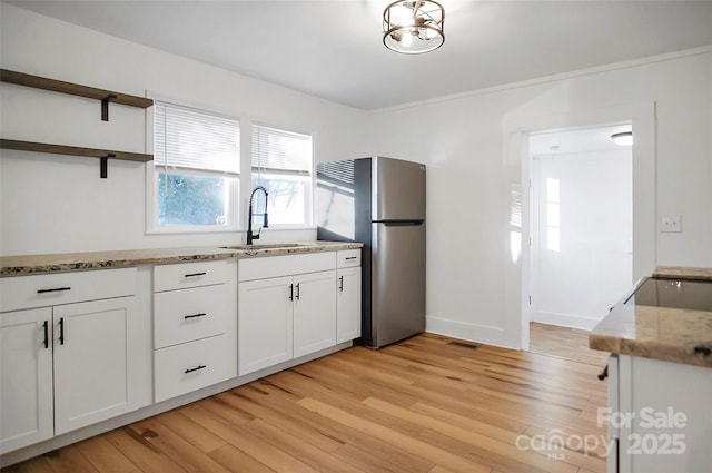 kitchen featuring white cabinets, stainless steel fridge, light wood-type flooring, and sink