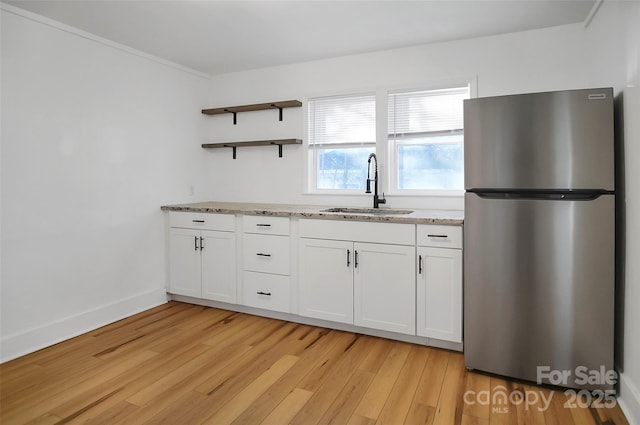 kitchen with white cabinets, sink, light wood-type flooring, light stone counters, and stainless steel refrigerator