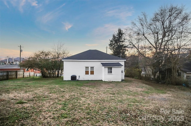 back house at dusk with a lawn and central AC unit