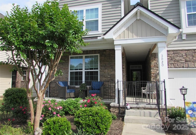 doorway to property featuring a porch, a garage, and stone siding