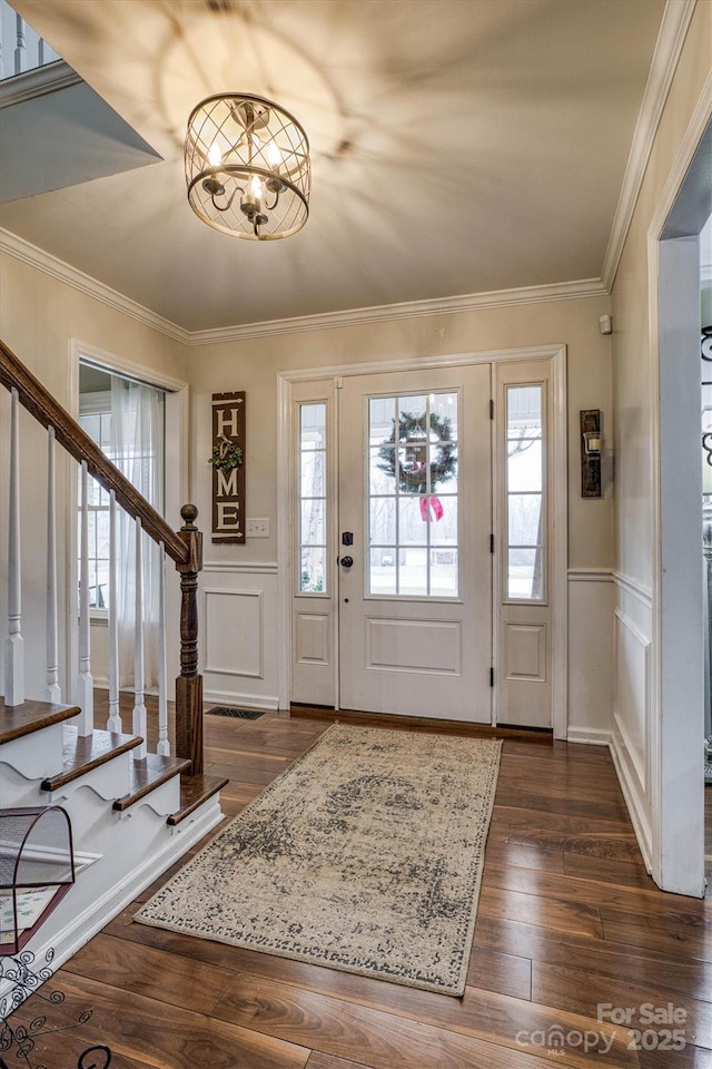 foyer entrance featuring dark hardwood / wood-style flooring, crown molding, and a chandelier