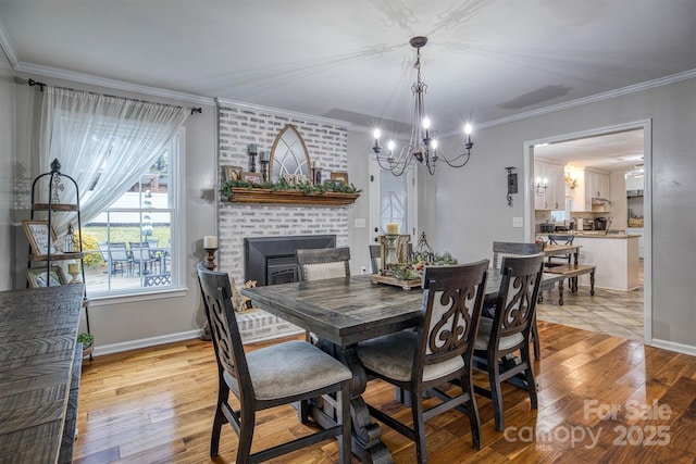 dining space featuring a fireplace, light wood-type flooring, a notable chandelier, and crown molding