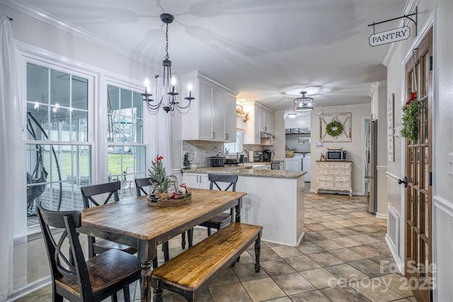 kitchen with washer and dryer, light stone countertops, white cabinetry, hanging light fixtures, and ornamental molding