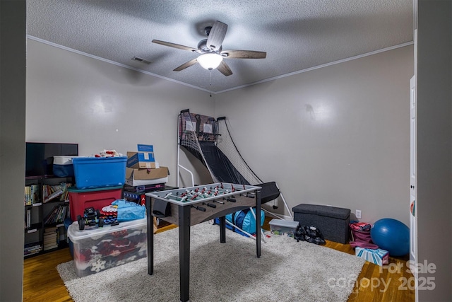 recreation room featuring ceiling fan, ornamental molding, a textured ceiling, and hardwood / wood-style floors