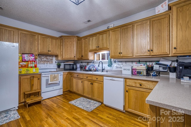 kitchen with a textured ceiling, sink, light wood-type flooring, and white appliances