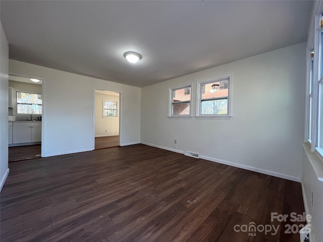 spare room featuring baseboards, visible vents, and dark wood-style flooring