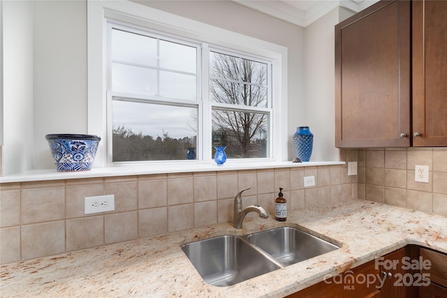 kitchen with tasteful backsplash, light stone counters, crown molding, and sink