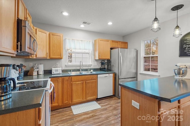 kitchen featuring a kitchen breakfast bar, stainless steel appliances, sink, light hardwood / wood-style flooring, and hanging light fixtures