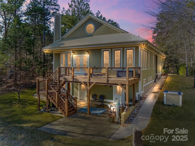 back house at dusk with a yard, a patio, and a wooden deck