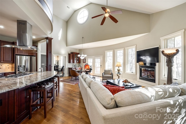 living room featuring ceiling fan with notable chandelier, high vaulted ceiling, plenty of natural light, and dark wood-type flooring