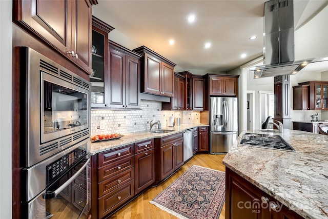 kitchen featuring light stone countertops, sink, stainless steel appliances, light hardwood / wood-style floors, and island range hood