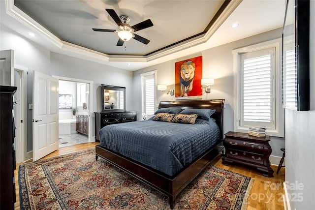 bedroom featuring ensuite bath, a tray ceiling, ceiling fan, crown molding, and wood-type flooring