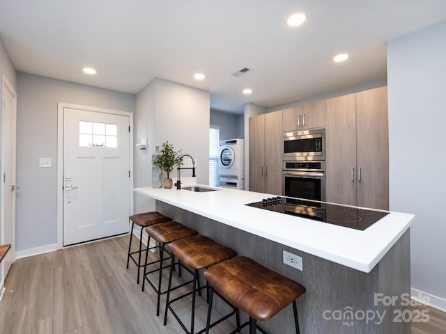 kitchen with stacked washer / drying machine, appliances with stainless steel finishes, a sink, a peninsula, and a kitchen breakfast bar