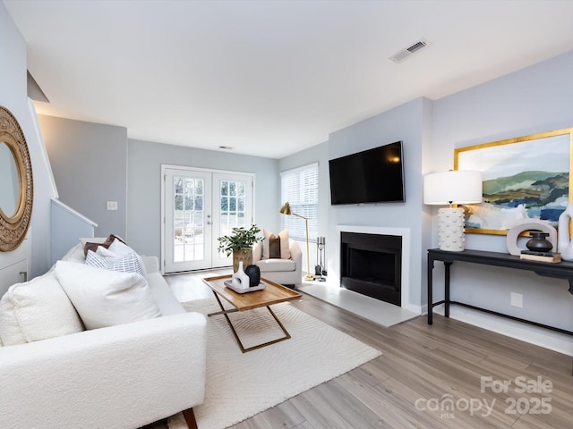 living area featuring a fireplace with flush hearth, visible vents, wood finished floors, and french doors