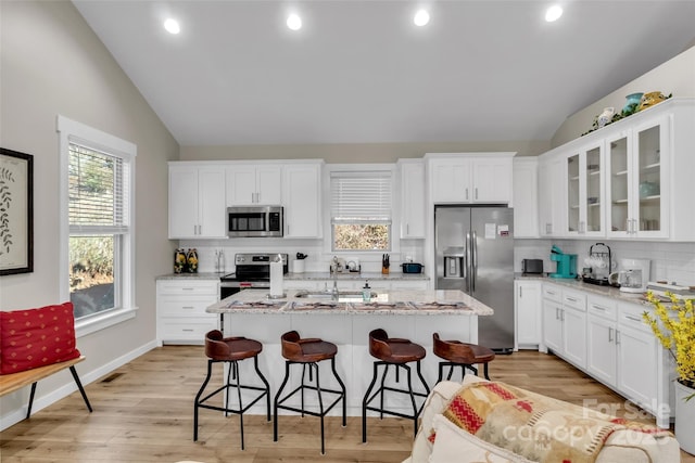 kitchen featuring a center island with sink, appliances with stainless steel finishes, lofted ceiling, and tasteful backsplash