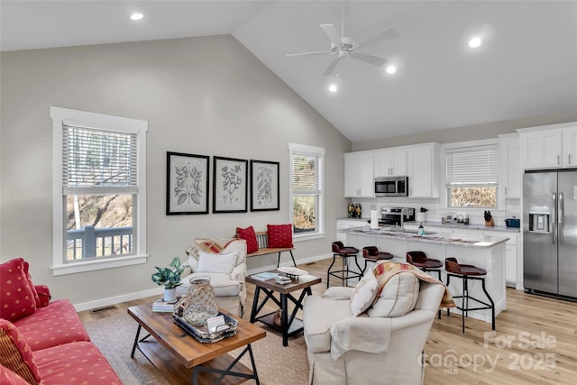 living room with light wood-type flooring, ceiling fan, a healthy amount of sunlight, and high vaulted ceiling