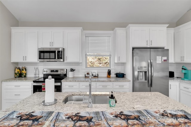 kitchen with backsplash, sink, white cabinetry, appliances with stainless steel finishes, and light stone counters