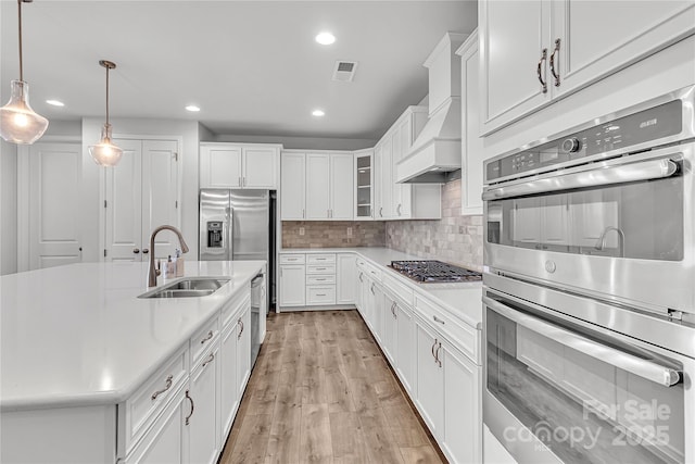 kitchen featuring sink, premium range hood, pendant lighting, white cabinetry, and stainless steel appliances