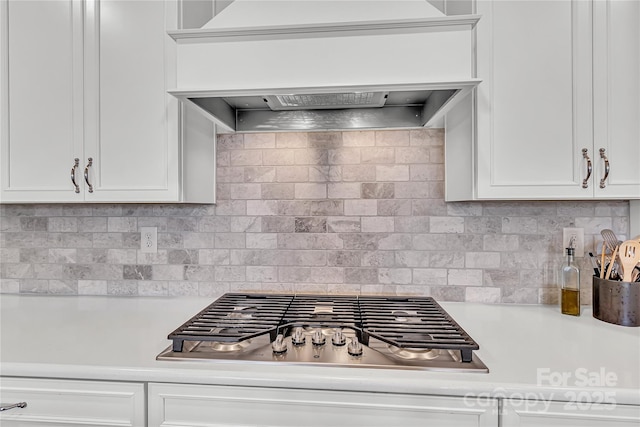 kitchen featuring white cabinets, decorative backsplash, custom exhaust hood, and stainless steel gas stovetop