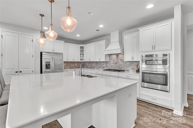 kitchen featuring sink, premium range hood, stainless steel appliances, white cabinets, and hanging light fixtures