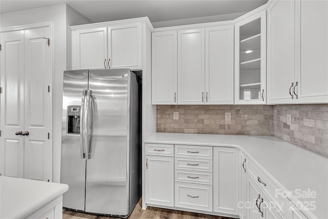 kitchen with white cabinets, light hardwood / wood-style floors, stainless steel fridge, and decorative backsplash