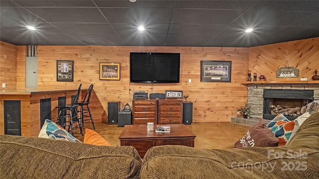 living room with electric panel, a drop ceiling, a fireplace, and wooden walls