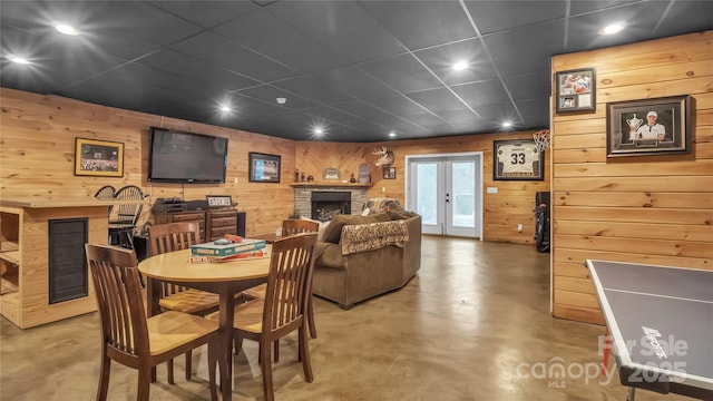 dining space featuring a stone fireplace, wooden walls, and concrete floors