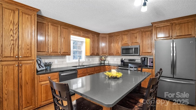 kitchen featuring sink, a textured ceiling, appliances with stainless steel finishes, tasteful backsplash, and a kitchen island