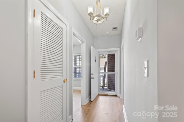 hallway with light wood-type flooring, a textured ceiling, and a notable chandelier