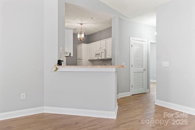 kitchen featuring pendant lighting, light hardwood / wood-style flooring, a chandelier, white cabinetry, and lofted ceiling