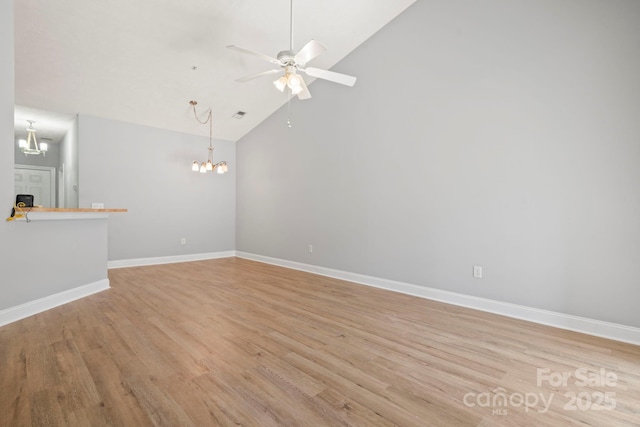 empty room featuring ceiling fan with notable chandelier, light hardwood / wood-style floors, and high vaulted ceiling