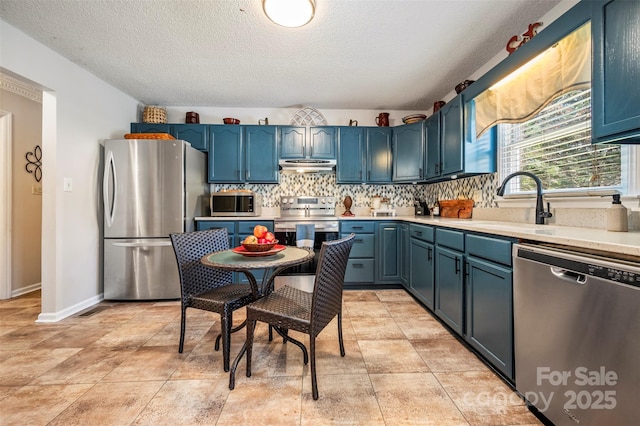 kitchen with appliances with stainless steel finishes, backsplash, a textured ceiling, blue cabinets, and sink