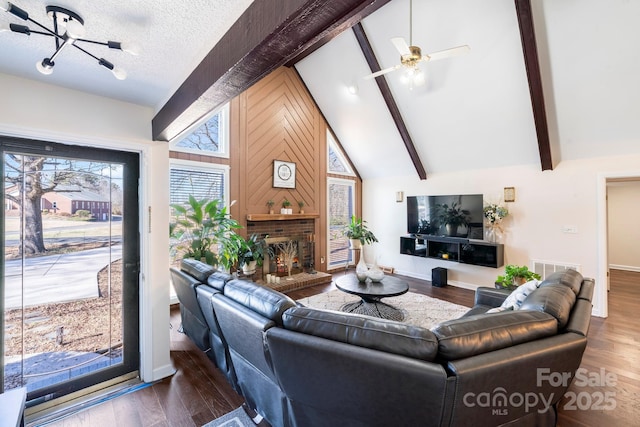 living room featuring a textured ceiling, dark hardwood / wood-style floors, beam ceiling, ceiling fan with notable chandelier, and a fireplace