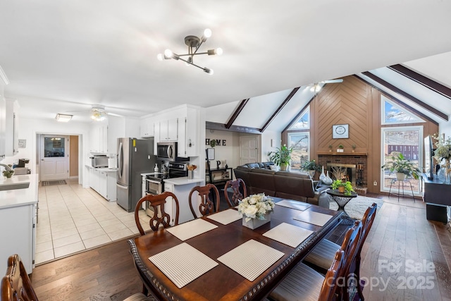 dining room with ceiling fan with notable chandelier, a brick fireplace, vaulted ceiling, and light hardwood / wood-style flooring