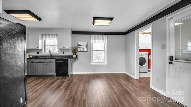 kitchen featuring a healthy amount of sunlight, black appliances, washer / dryer, dark hardwood / wood-style floors, and white cabinetry