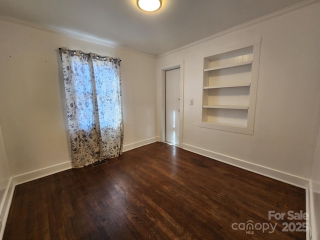 empty room with dark wood-type flooring, built in features, and ornamental molding