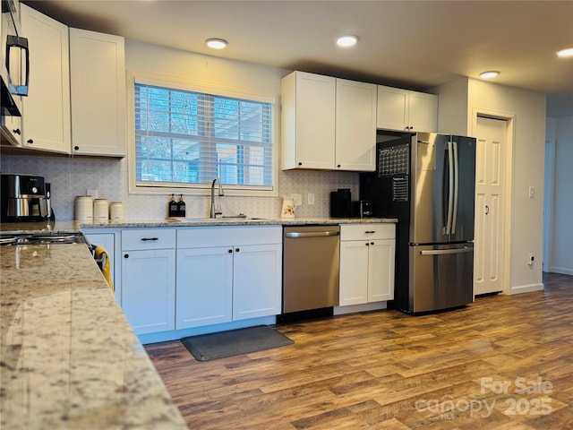 kitchen featuring white cabinetry, appliances with stainless steel finishes, wood-type flooring, light stone countertops, and sink