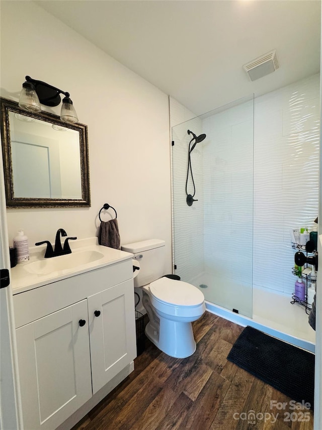 bathroom featuring toilet, a tile shower, wood-type flooring, and vanity