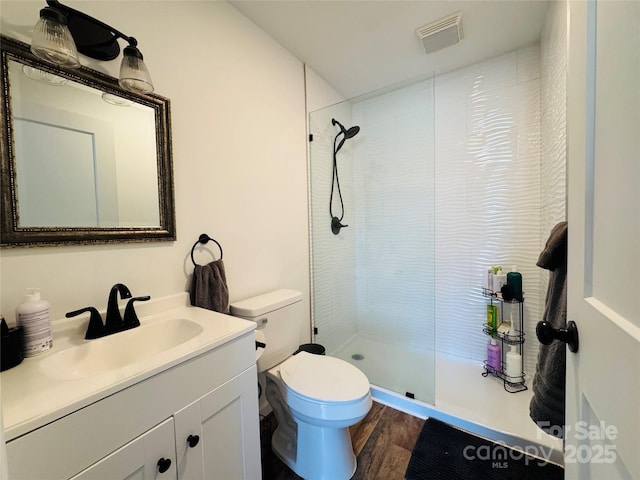 bathroom featuring toilet, wood-type flooring, tiled shower, and vanity